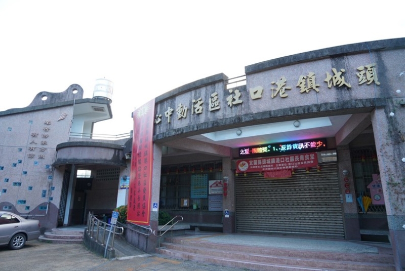 港口社區活動中心外牆是粉紅色洗石子牆面，左邊牆面上有「牽罟倚索就分魚，有人有份」的字樣。